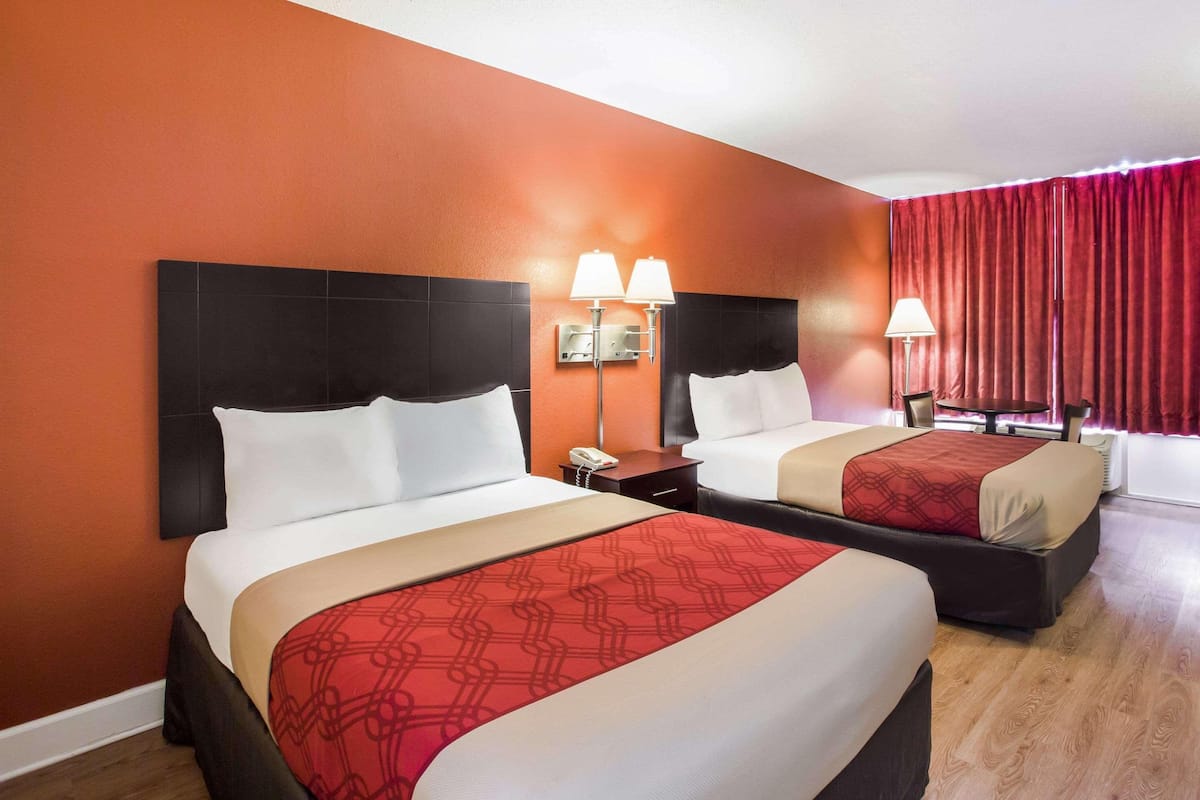 Habitación de hotel con dos camas, una mesita de noche con un teléfono y una ventana con cortinas rojas.