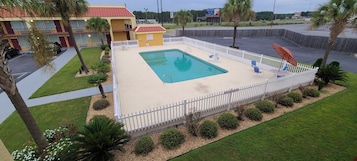 Una piscina con cerca blanca, rodeada de palmeras y un césped.