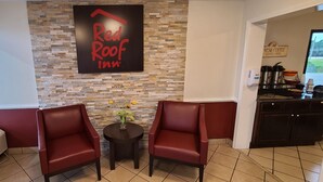 Zona de estar de Red Roof Inn con dos sillones de cuero rojo, una mesita con un florero y una pared de piedra.