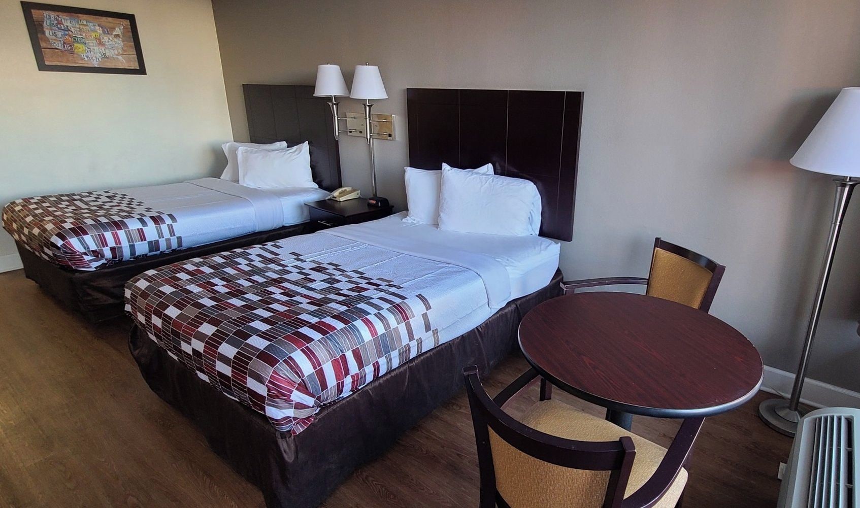 A hotel room with two beds, a bedside table with lamps, a round wooden table, and a chair.