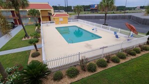 Una piscina rodeada por una valla blanca, con un edificio al fondo.