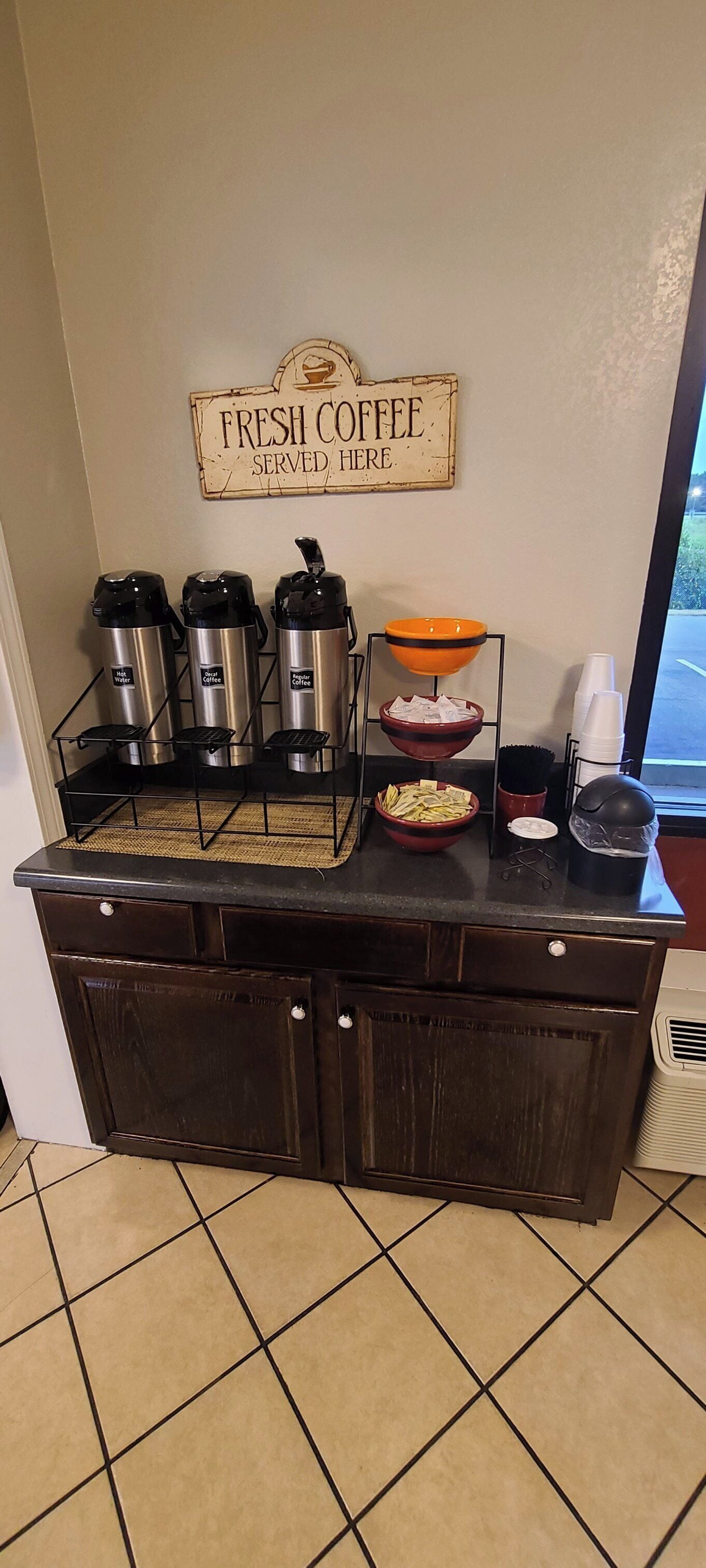 A coffee station with three coffee dispensers, a bowl of cash, and a sign that reads 'FRESH COFFEE SERVED HERE.'