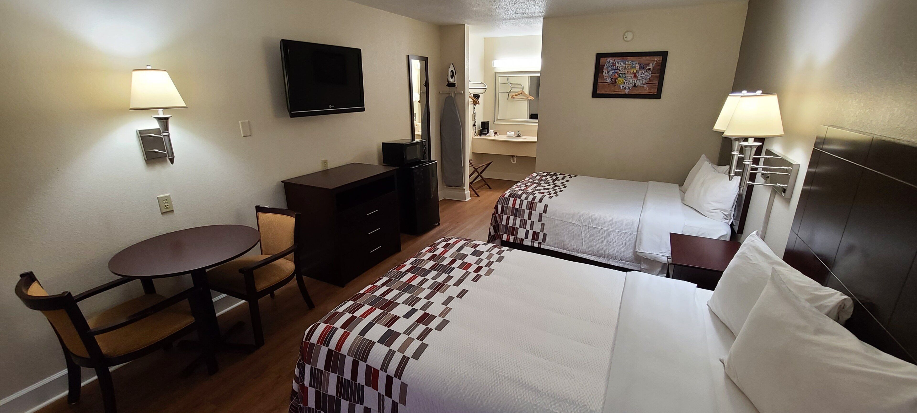 A hotel room with two beds, a desk, a chair, a television, and a bathroom visible through an open door.