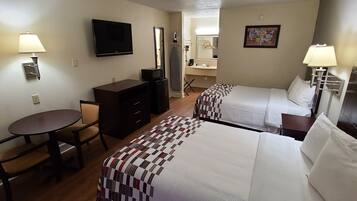A hotel room with two beds, a desk, a chair, a television, and a bathroom visible through an open door.