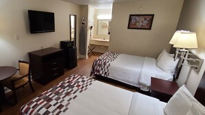 A hotel room with two beds, a desk, a television, a mirror, a bathroom, and a painting on the wall. - Red Roof Inn Tifton (Tifton)
