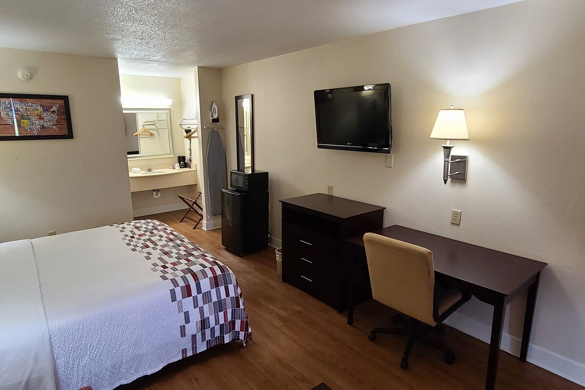 A hotel room with a bed, desk, TV, and a mirror.
