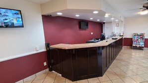 Un área de recepción con un mostrador oscuro, un televisor montado en la pared y un ventilador de techo.