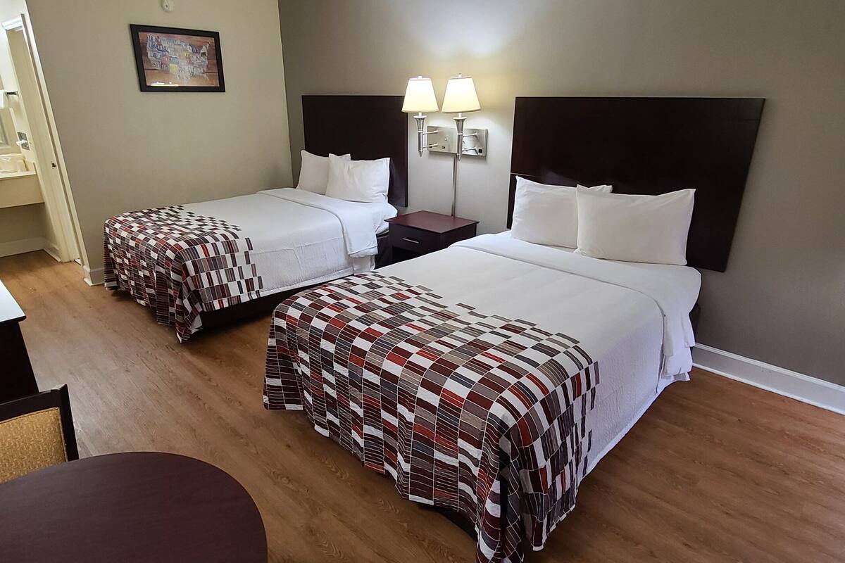 Ein Hotelzimmer mit zwei Betten, einem Schreibtisch, einem Stuhl, einem kleinen Tisch und einem Spiegel.