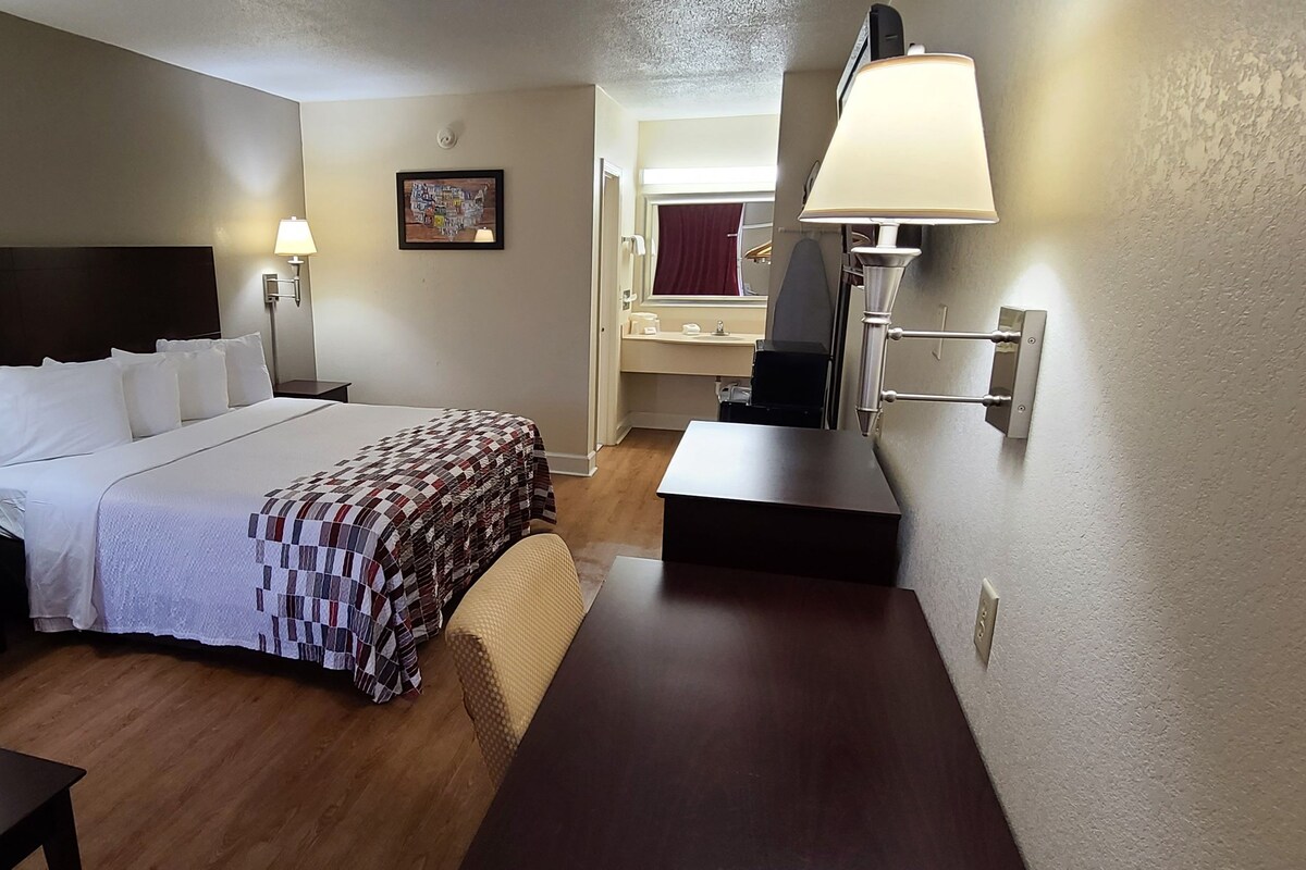 Quarto de hotel com uma cama, um sofá, uma mesa de trabalho e um banheiro visível por uma porta aberta.