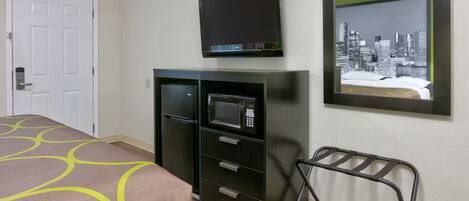 A hotel room with a bed, a minibar, a television, and a cityscape view.
