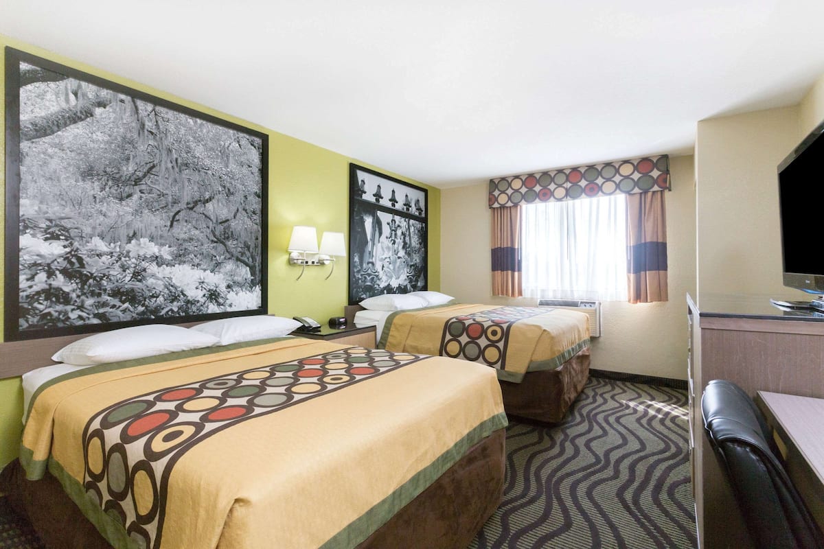 A hotel room with two beds, a desk, a television, and a large framed picture on the wall.
