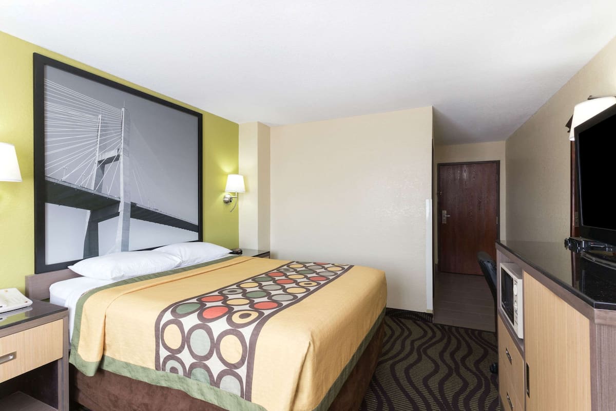 A hotel room with a bed, a desk, a television, and a door leading to another room.
