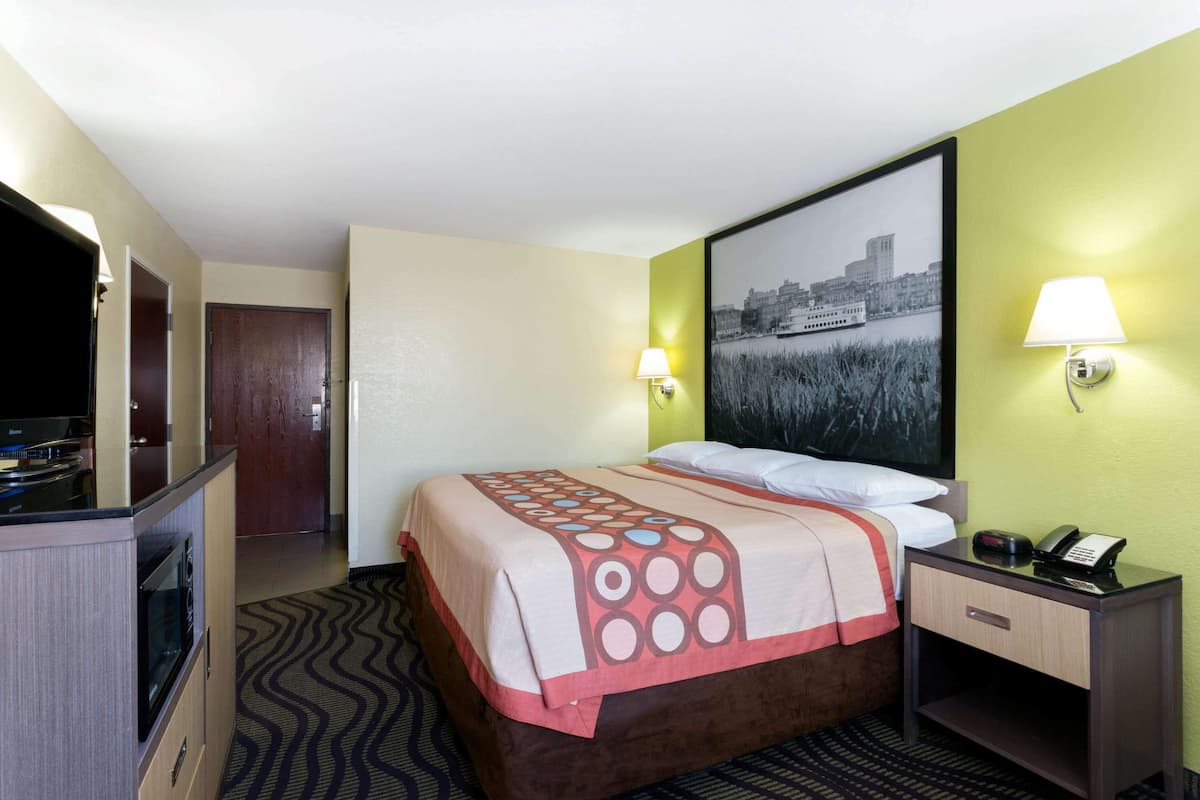 A hotel room with a bed, a desk, a lamp, and a painting on the wall.
