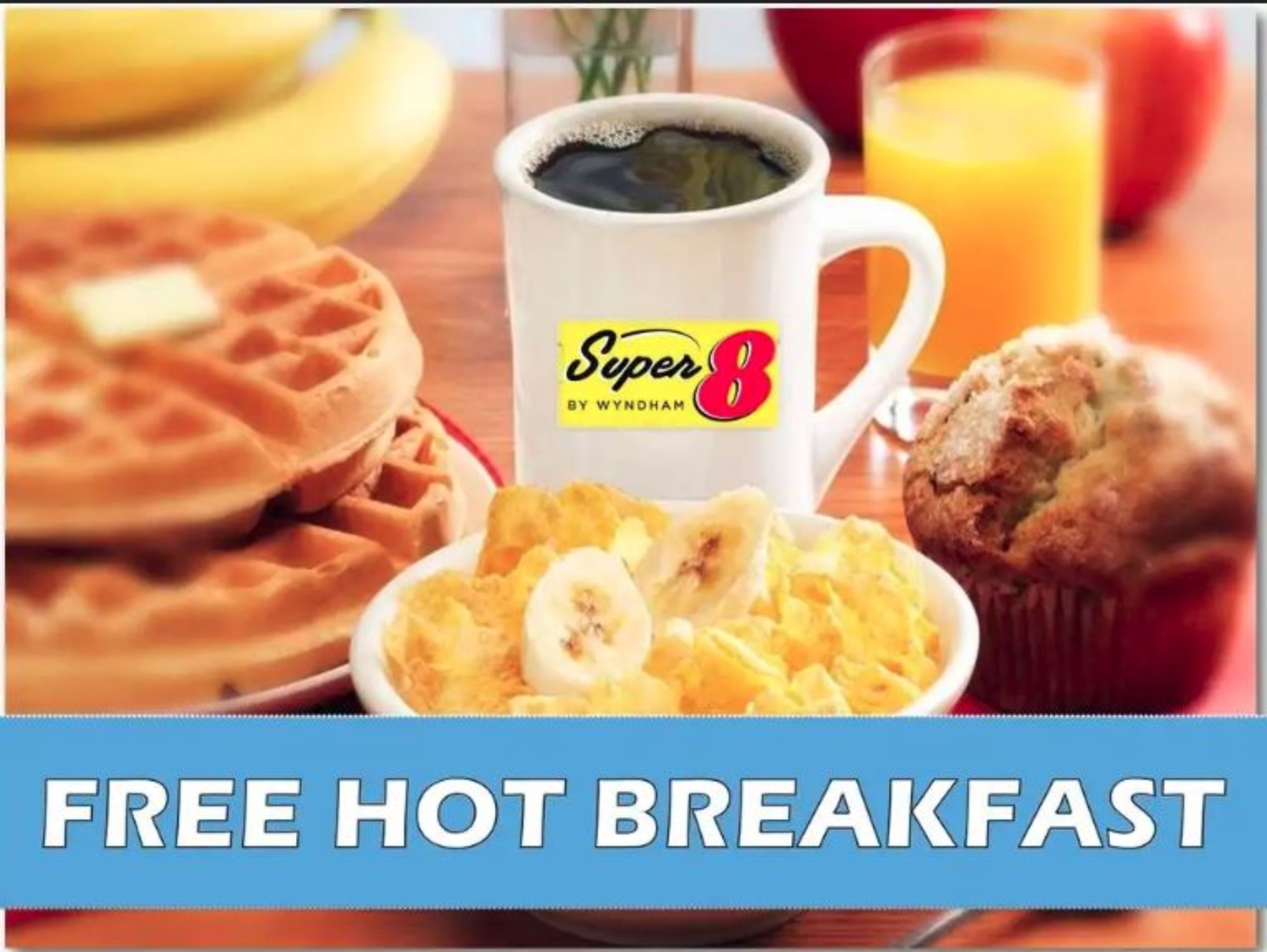 Une table dressée pour le petit-déjeuner avec des gaufres, un muffin, un bol de céréales aux bananes, une tasse de café et un verre de jus d’orange.