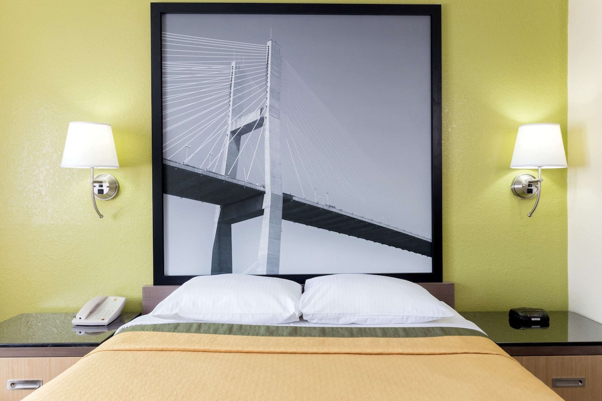 A hotel room with a bed, a nightstand with a phone, and a wall-mounted lamp.