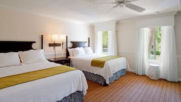 A hotel room with two beds, a ceiling fan, a window with curtains, and a view of the outdoors.