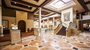 A spacious lobby with a grand staircase, a high ceiling with skylights, and a large painting on the wall. - The King and Prince Beach & Golf Resort (St. Simons Island)