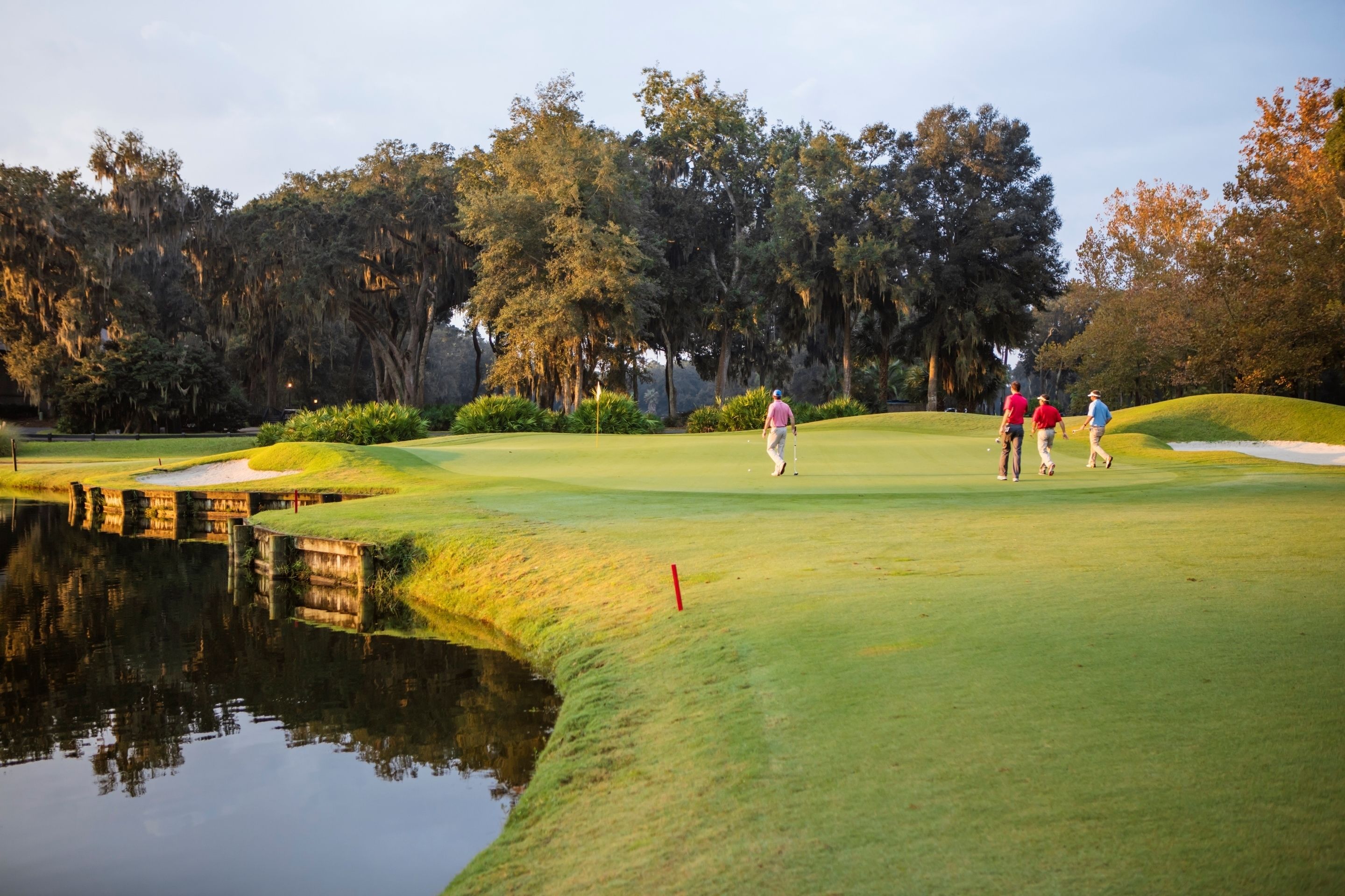 A golf course with a water body, trees, and a sand bunker.