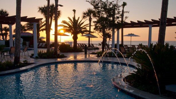 A pool area with lounge chairs and umbrellas, surrounded by palm trees and a sunset view. - The King and Prince Beach & Golf Resort (St. Simons Island)