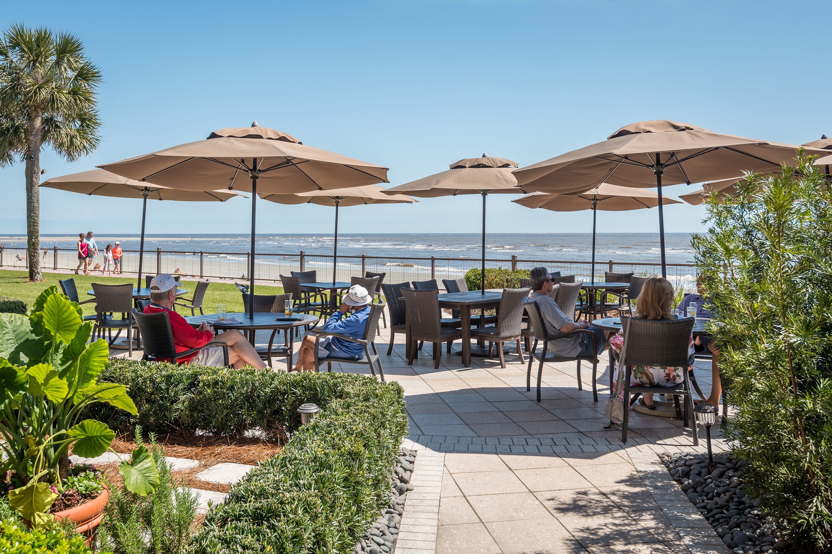 An outdoor patio with tables and chairs under umbrellas, overlooking the beach.