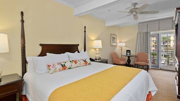 A hotel room with a four-poster bed, a ceiling fan, a view of the outside balcony, and a small table with a lamp.