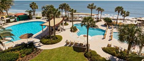 A resort pool area with multiple swimming pools, palm trees, and beach views.