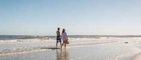 A beach scene with two people walking along the shore.