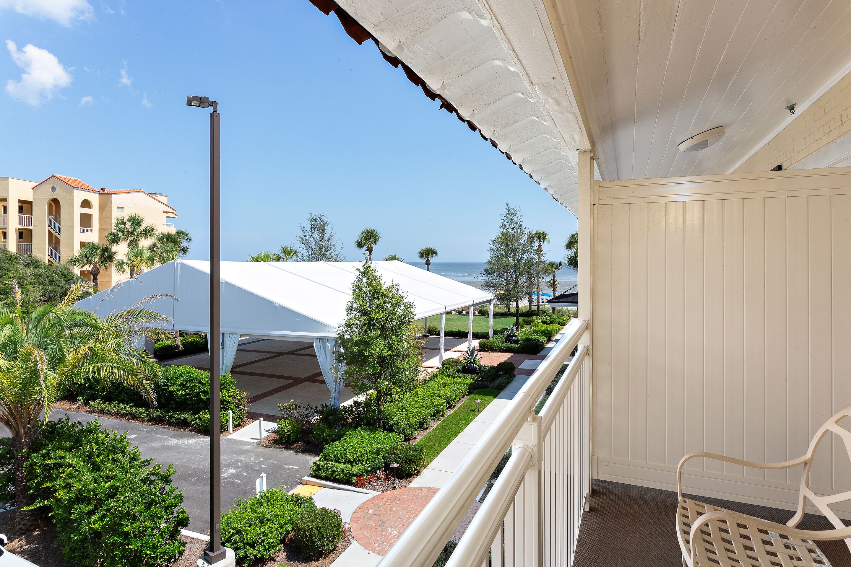 A balcony with a view of a landscaped area, a white building, and a clear sky.