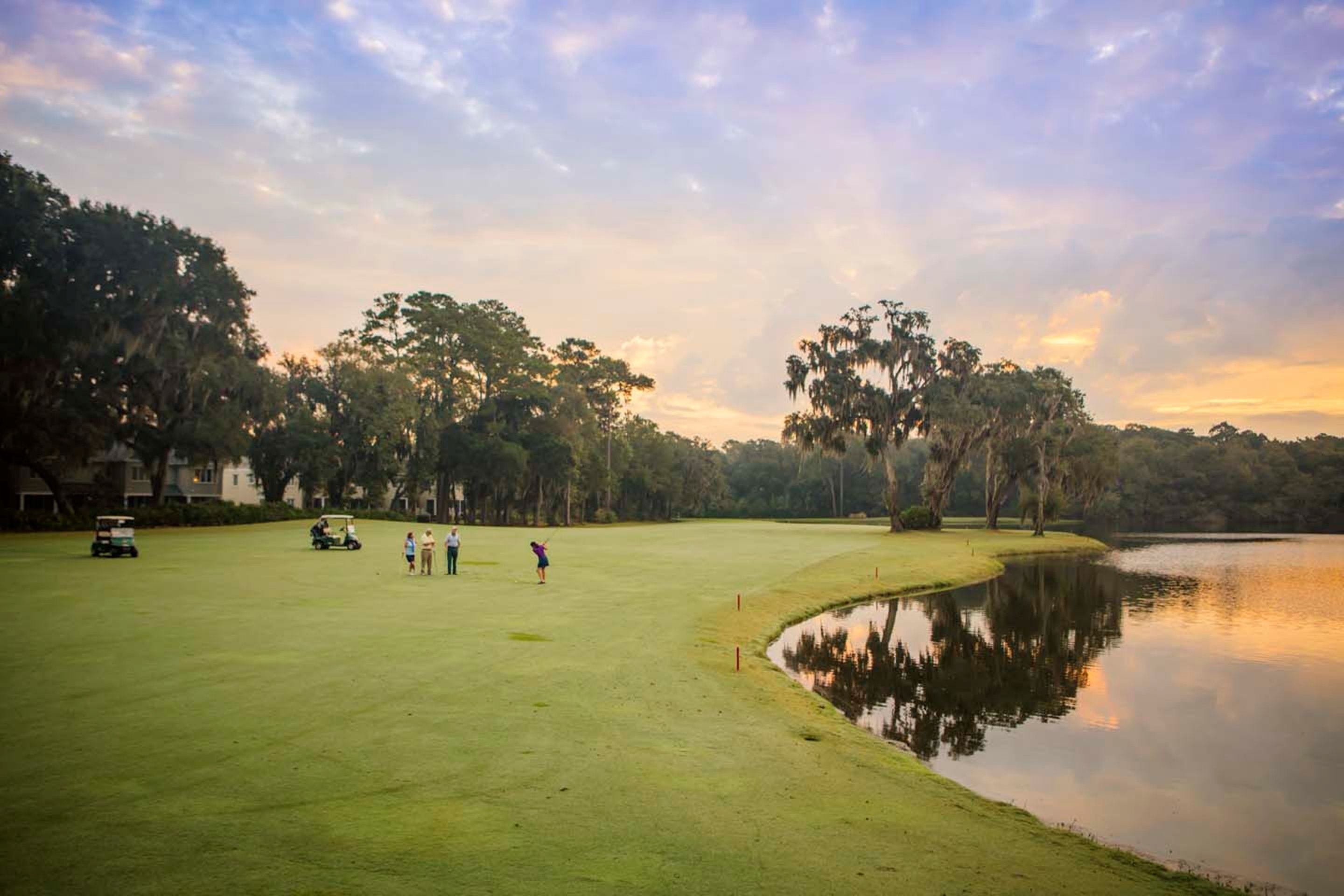 A golf course with a pond, surrounded by trees and a clear sky.