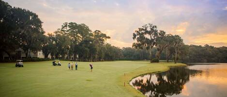 A golf course with a pond, surrounded by trees and a clear sky.