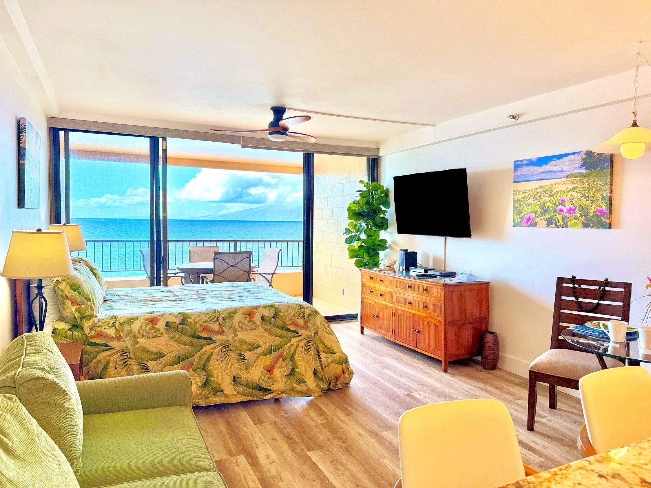 A hotel room with a bed, a television, a dining area, and a balcony with a view of the sea.