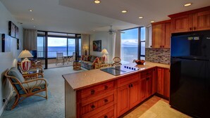 Cocina moderna con armarios de madera, un refrigerador negro y un comedor con sillas de mimbre y vista al océano.