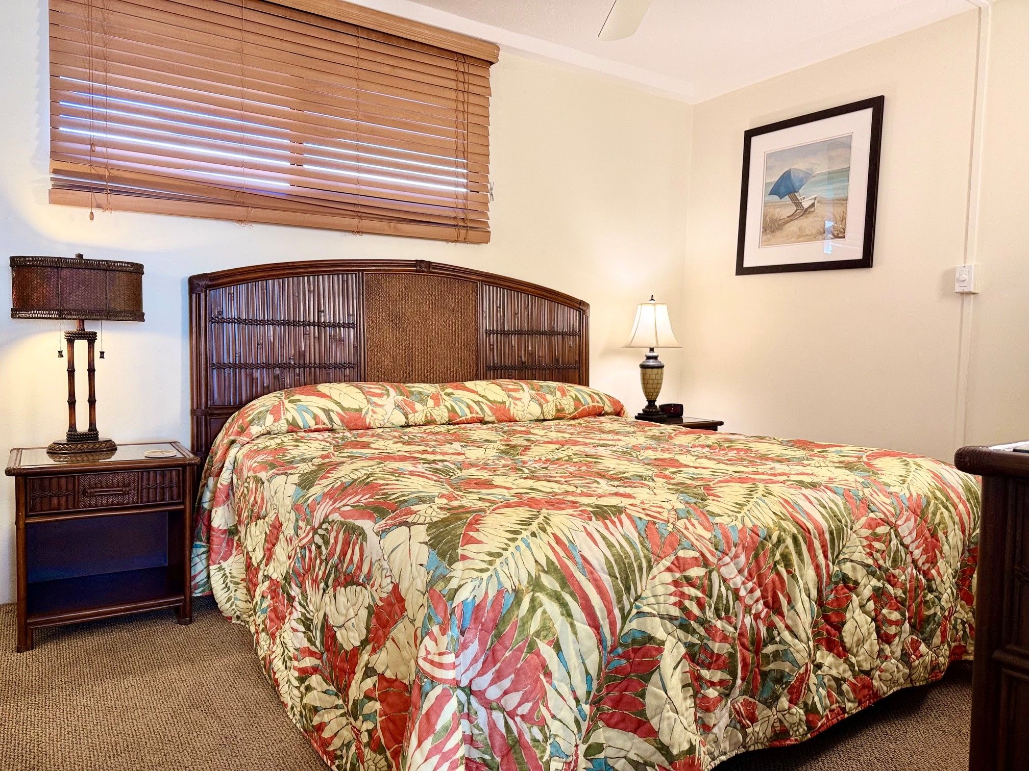 Habitación de hotel con una cama grande, dos mesitas de noche, una lámpara de pared y un cuadro enmarcado, además de un ventanal con persianas.