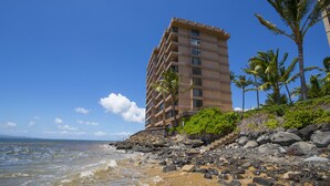 Un hotel frente a la playa con una estructura de varios pisos, costa rocosa y palmeras.