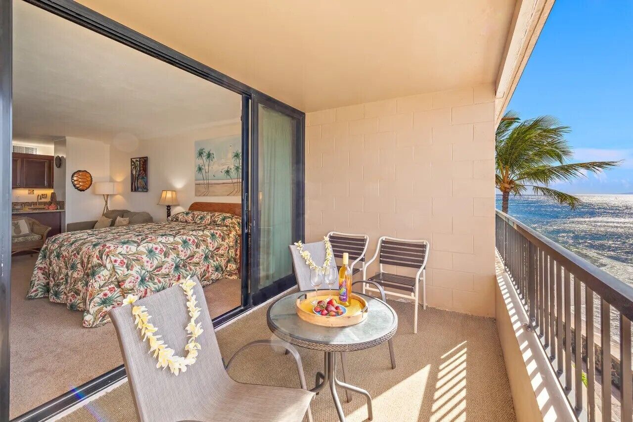 A balcony with a table set for two, a bed with floral bedding, and a view of the ocean.
