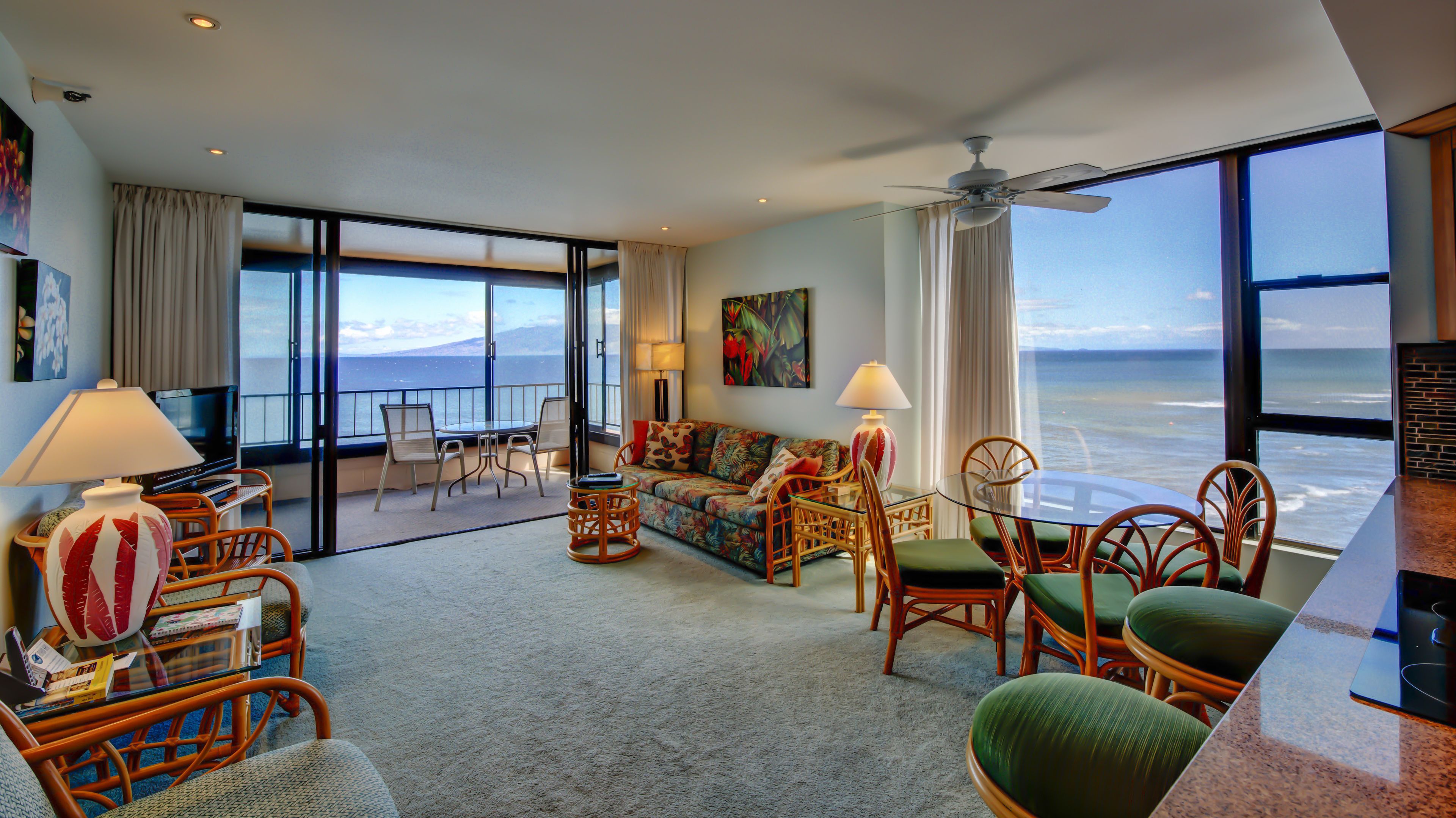 A spacious living room with a large window offering a view of the ocean, a sofa, chairs, and a dining table.