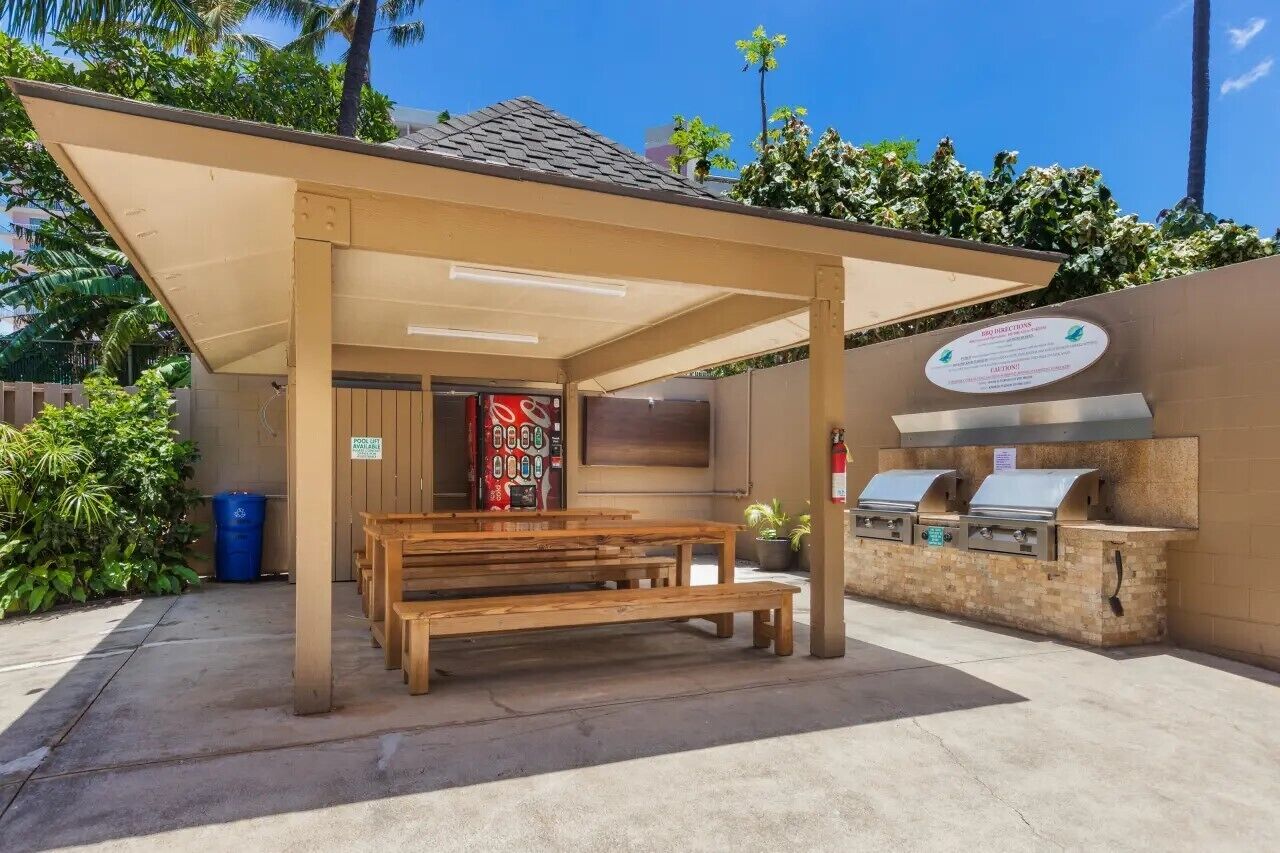An outdoor patio with a covered seating area, a barbecue grill, and a wall-mounted sign.