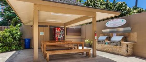An outdoor patio with a covered seating area, a barbecue grill, and a wall-mounted sign.