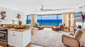 Un espacio habitable amplio con cocina, ventanas grandes con vista al océano y un ventilador de techo.