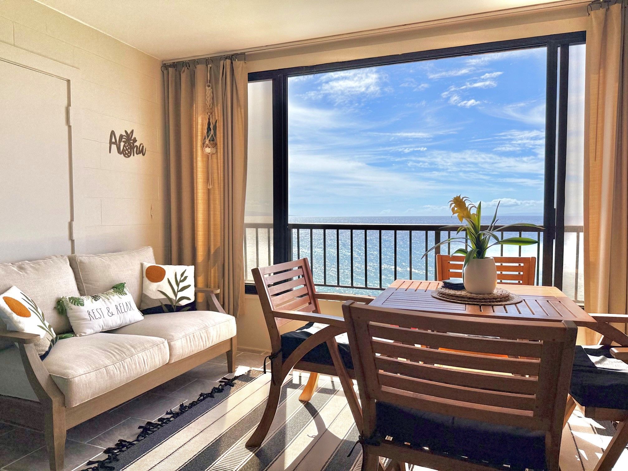 A balcony with a view of the ocean, a sofa with decorative pillows, and a wooden table with chairs.