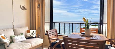 A balcony with a view of the ocean, a sofa with decorative pillows, and a wooden table with chairs.