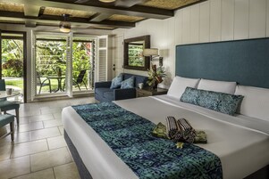 A spacious bedroom with a large bed, a nightstand, a lamp, and a view of a lush garden through a sliding glass door.