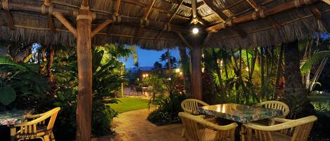 An outdoor patio with a thatched roof, wicker furniture, and tropical plants.