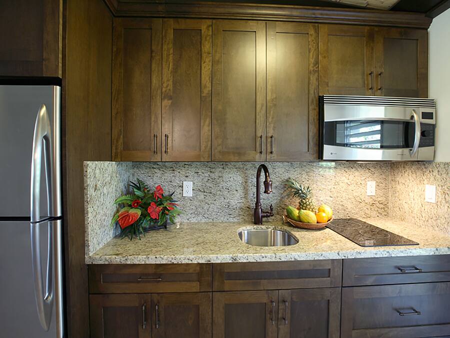 A kitchen with wooden cabinets, a stainless steel refrigerator, a microwave, and a granite countertop.