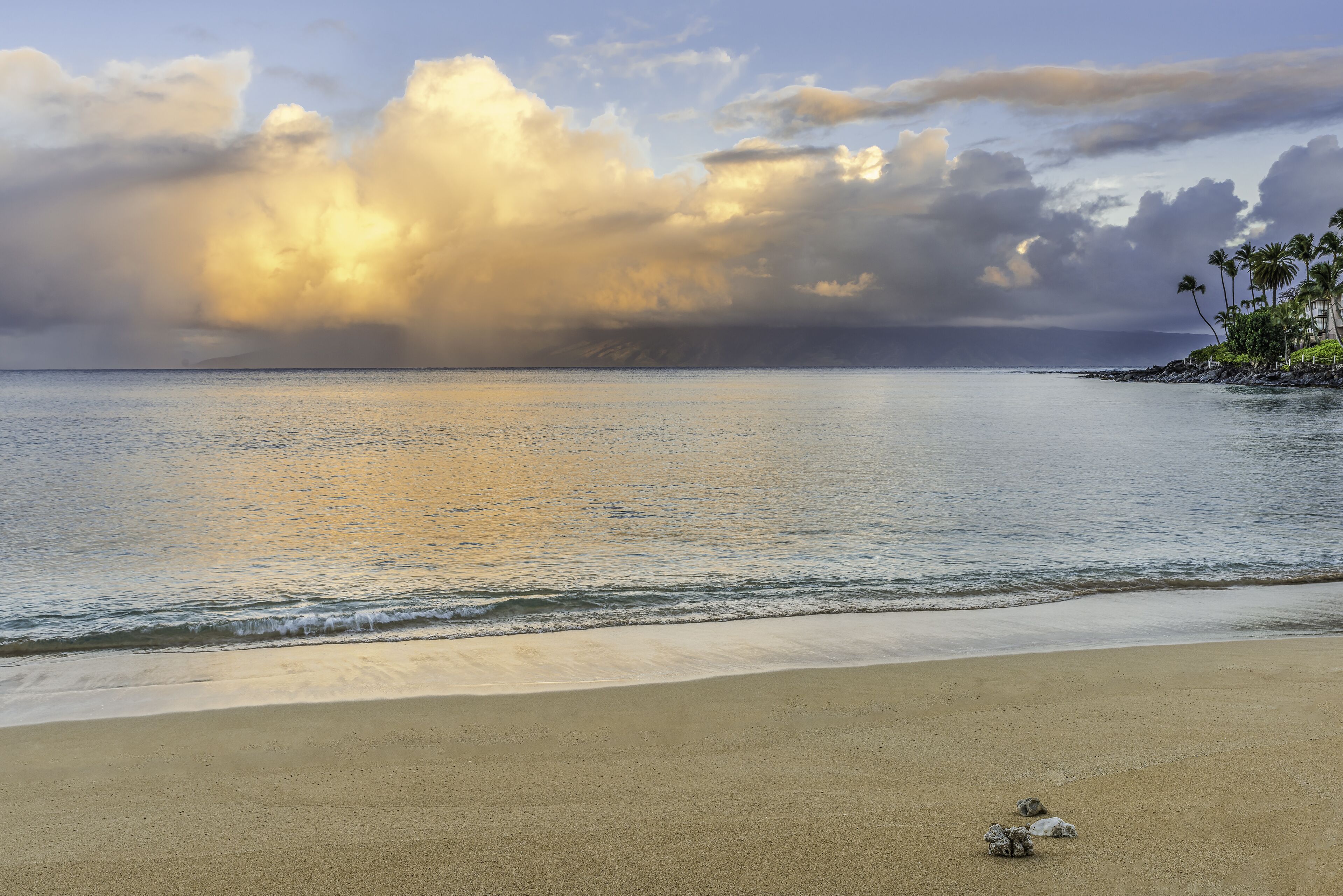 A beach with calm waters, a sandy shore, and a cloudy sky.