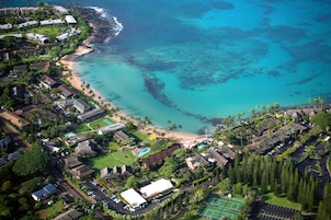 Vista aérea de um resort costeiro com propriedades na praia, quadra de tênis e vegetação exuberante.
