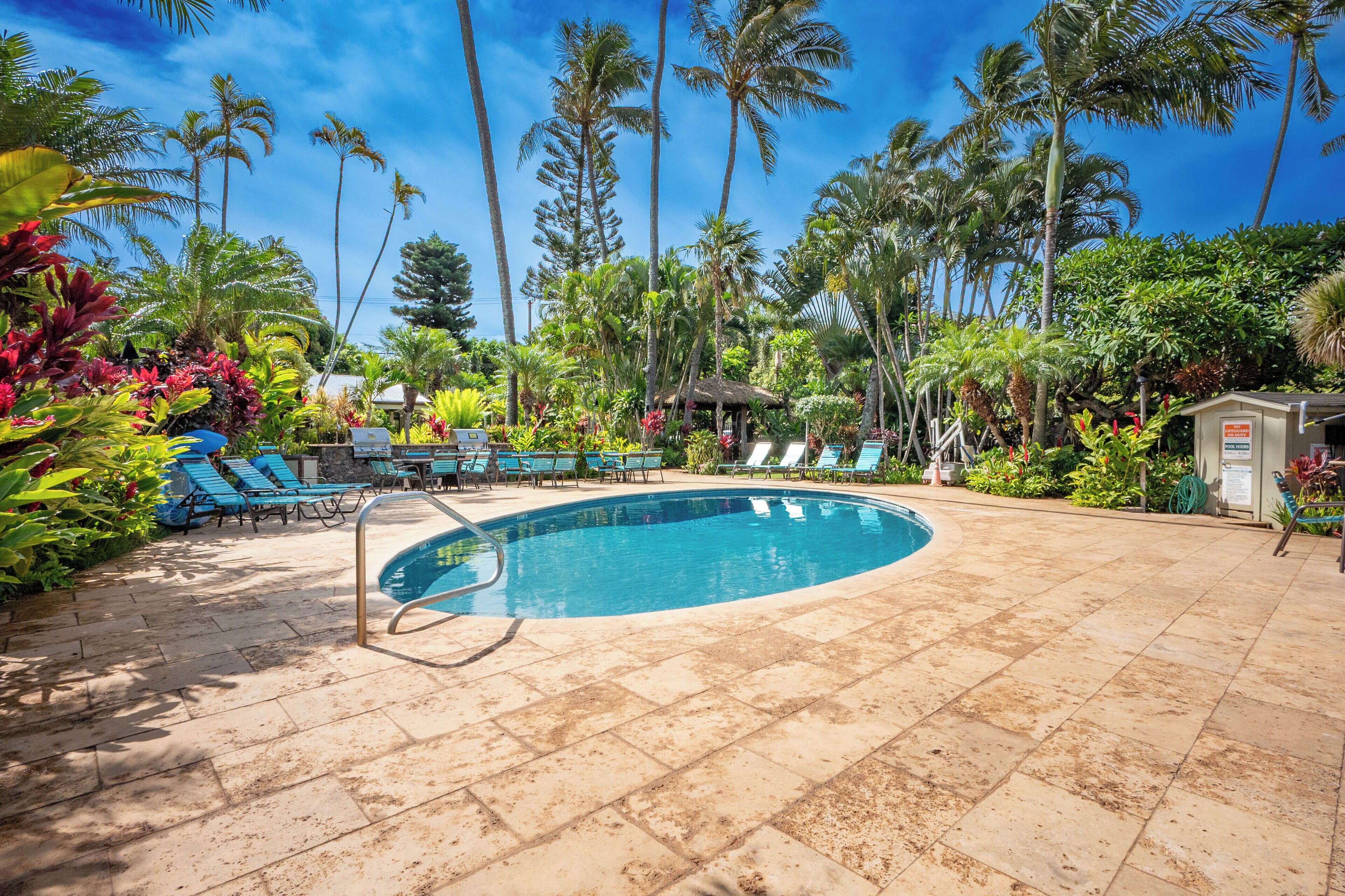 A pool area with lounge chairs, palm trees, and a small hut.