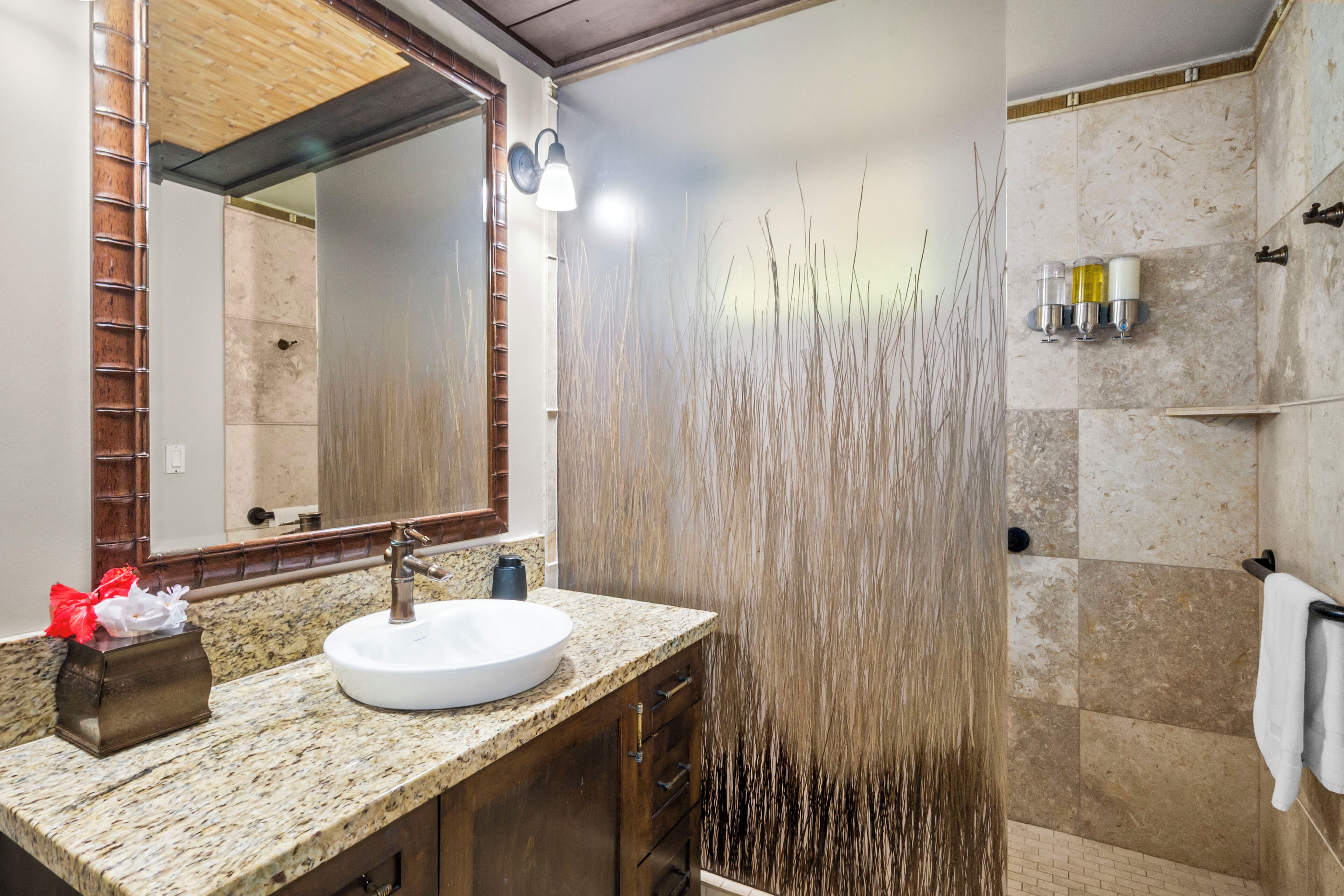 A bathroom with a granite countertop, a white sink, a mirror, and a shower with a vertical water feature.