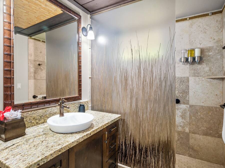 A bathroom with a granite countertop, a white sink, a mirror, and a shower with a vertical water feature.