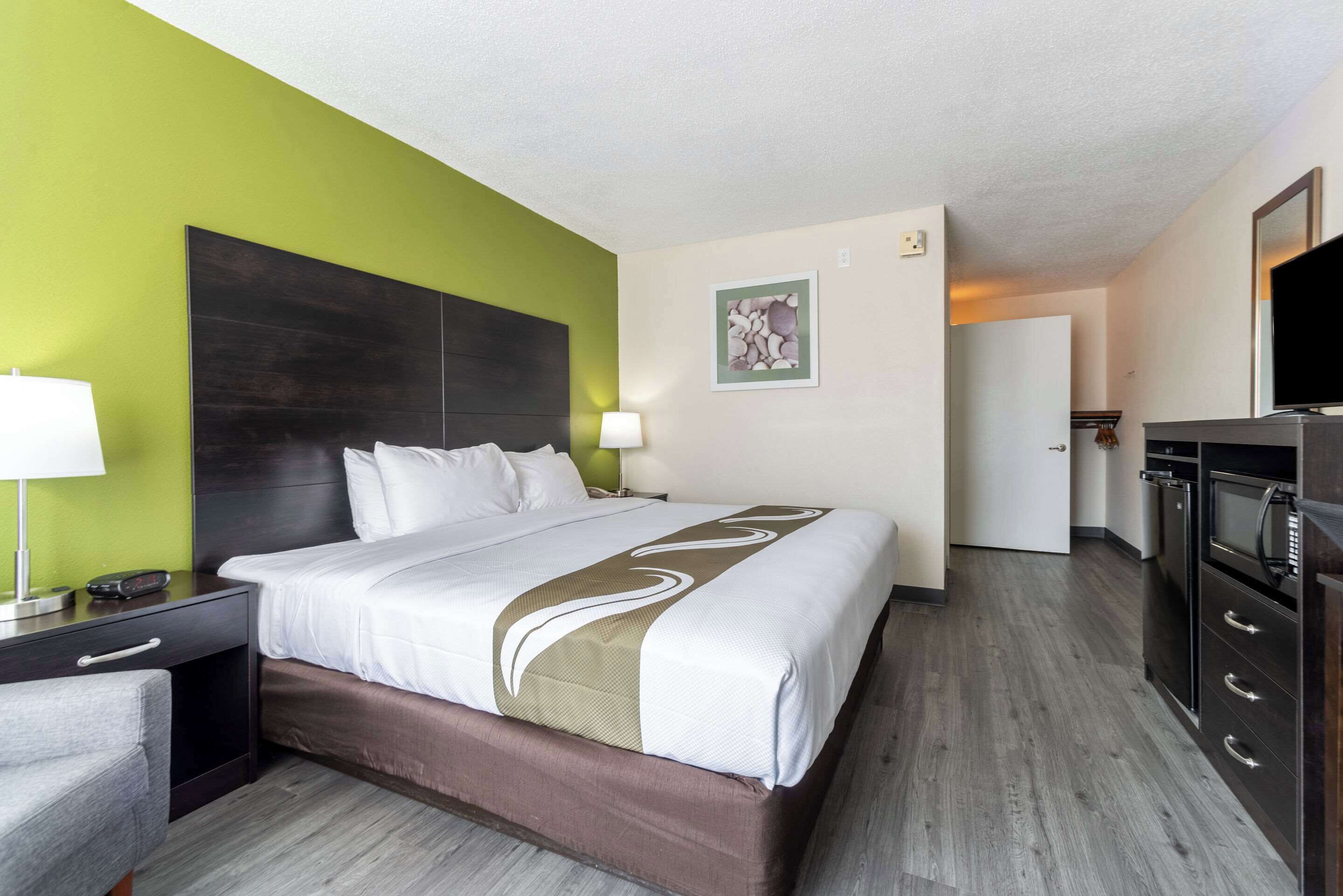 Une chambre d’hôtel comprenant un grand lit, une table de chevet, un bureau, une chaise, une télévision et une kitchenette.